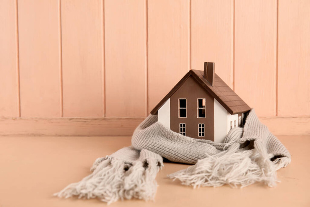 Huis model met sjaal op beige houten achtergrond. Verwarmingsconcept - Foto, afbeelding