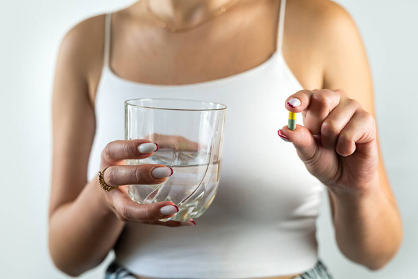 Niezdrowa chora kobieta cierpiąca na bezsenność lub ból głowy i zażywająca tabletki nasenne popijając szklanką wody. Dziewczyna trzyma środek przeciwbólowy na ból. zbliżenie izolowane - Zdjęcie, obraz