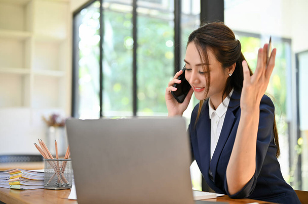 Güzel ve profesyonel Asyalı iş kadını müşterisiyle telefonda konuşuyor, masasında çalışırken telefonla iş anlaşması yapıyor.. - Fotoğraf, Görsel