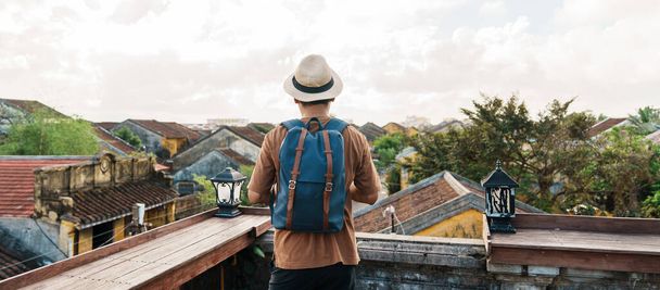 Hoi 'de seyahat eden mutlu bir solo gezgin Vietnam' daki antik bir kasabada sırt çantasıyla çatı manzaralı bir adam. Şehir simgesi ve turistik yerleriyle ünlüdür. Vietnam ve Güneydoğu Asya seyahat kavramı - Fotoğraf, Görsel