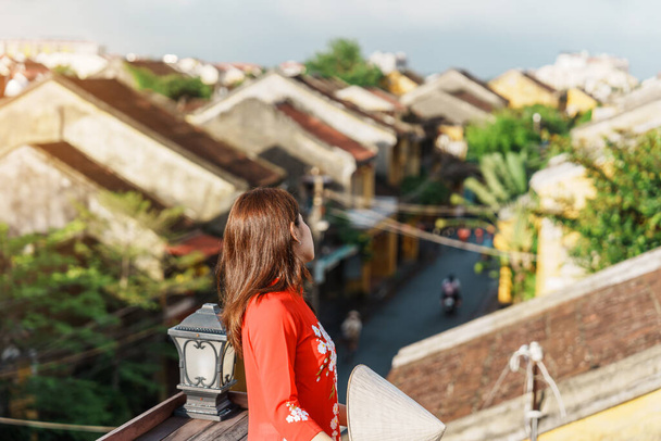 mujer feliz vistiendo vestido vietnamita Ao Dai, vista de turismo viajero en la azotea en Hoi Una antigua ciudad. hito y popular para las atracciones turísticas. Vietnam y el sudeste concepto de viaje - Foto, Imagen