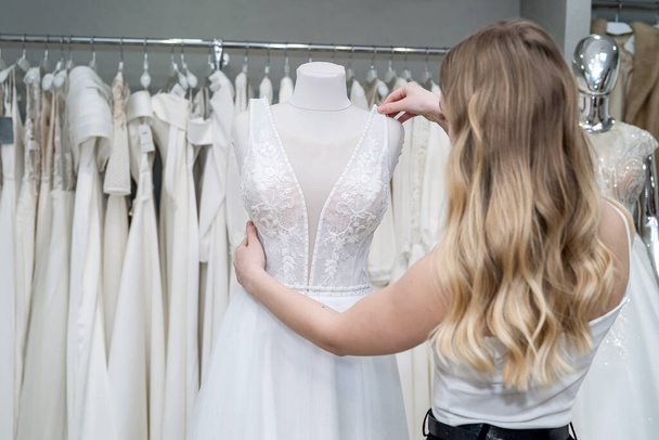 pretty bride look and touch white wedding dresses while being in the wedding boutique - Photo, Image