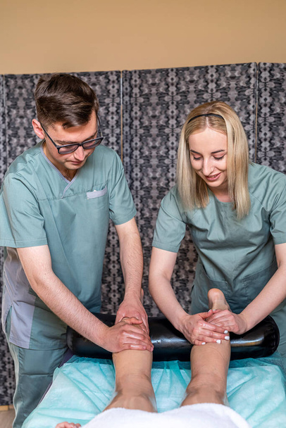 Twee massagetherapeuten een vrouw en een moeder geven een dubbele voet- en beenmassage aan een meisje in een spa salon. Vier handen van masseur tijdens massage close-up - Foto, afbeelding