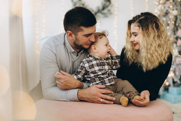 Portret szczęśliwej rodziny ojca matki i małego kręconego synka świętujących Boże Narodzenie razem w domu. Koncepcja sylwestrowa. - Zdjęcie, obraz