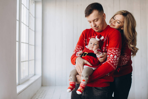 Portrait de maman de famille heureuse papa et petite fille en rouge vêtements de Noël traditionnels passer du temps ensemble dans la pièce en bois léger près de la fenêtre, espace de copie - Photo, image