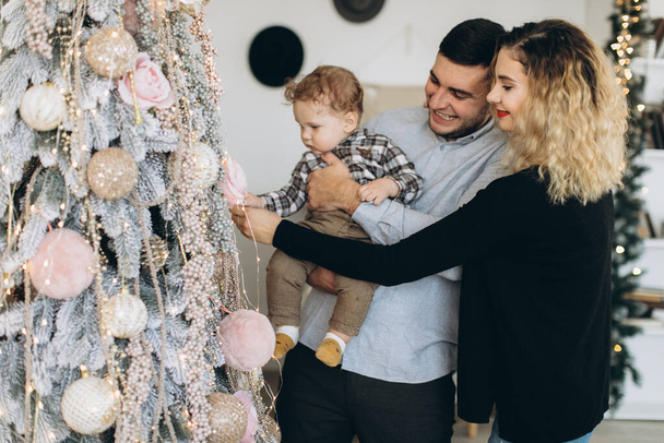 家庭で一緒にクリスマスを祝う父親の母親と小さな巻き毛の息子の幸せな家族の肖像画。大晦日のコンセプト. - 写真・画像