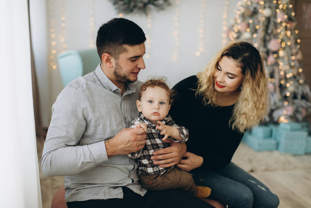 Portrait of happy family of father mother and little curly son celebrating Christmas together at home. New Year`s Eve concept. - Фото, изображение
