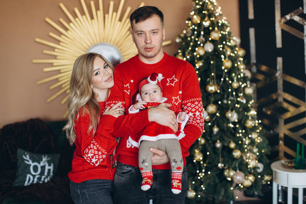 幸せな家族のお母さんお父さんと小さな娘で赤伝統的なクリスマス服一緒に過ごす時間近くクリスマスツリー、コピースペース - 写真・画像