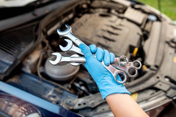 automonteur repareert een automotor in een garage met een moersleutel. auto-onderhoud. Reparatie. - Foto, afbeelding