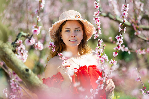 Cheerful girl posing in a red dress in a spring blooming garde - Foto, Imagen