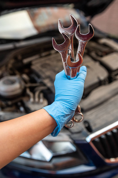 Araba tamircisi bir araba atölyesinde ingiliz anahtarıyla araba motoru tamir ediyor. Araba bakımı. onarım hizmetleri. - Fotoğraf, Görsel