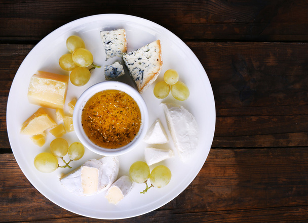 Different sort of cheese with grape and saucer on plate on wooden table background - 写真・画像
