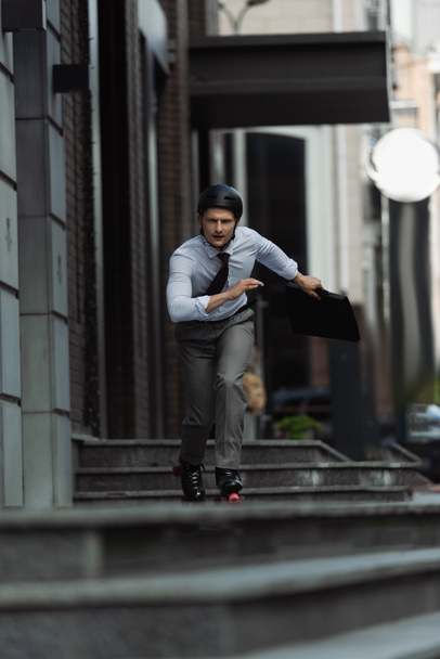 Молодой бизнесмен на роликовых коньках катается по лестнице на городской улице  - Фото, изображение