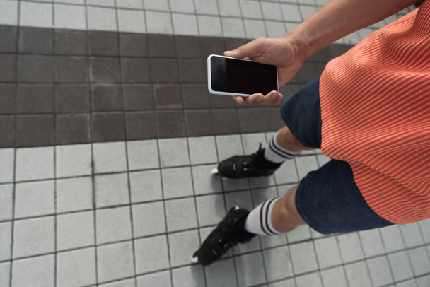 Visão superior do patinador de rolo segurando smartphone com tela em branco ao ar livre  - Foto, Imagem