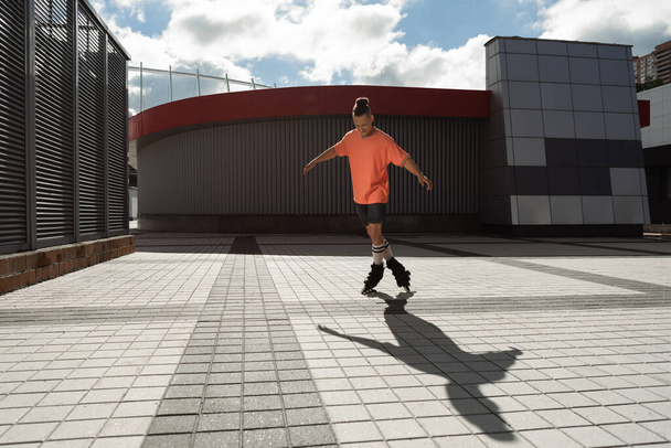 Young man in roller skates skating near buildings on urban street  - Foto, imagen
