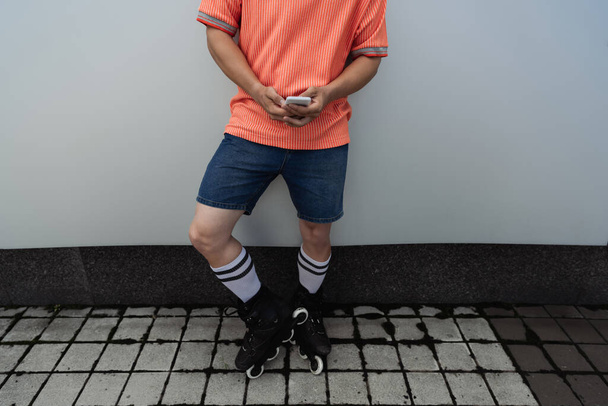 Cropped view of man in roller skates using cellphone near wall outdoors  - Fotoğraf, Görsel