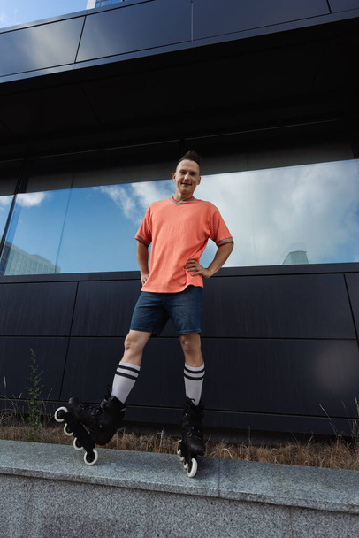 Wide angle view of smiling man in roller blades standing on parapet outdoors  - Photo, Image