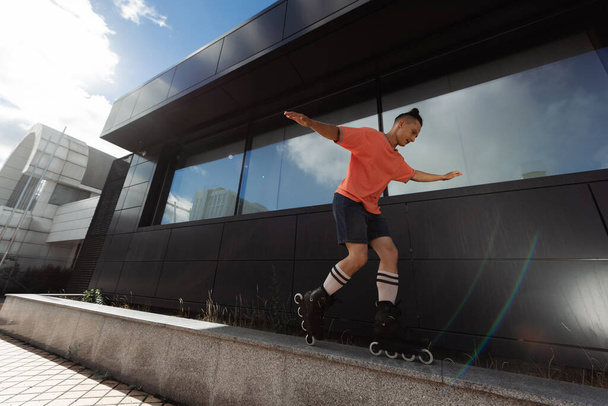 Junger Mann mit Rollerblades trickst auf Brüstung nahe Gebäude im Freien  - Foto, Bild