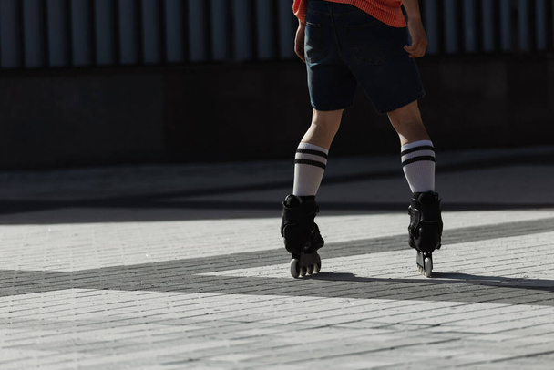 Cropped view of young man in shorts and roller skates riding on city square at daytime  - Foto, imagen