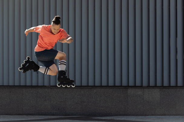 Homme en patins à roulettes sautant alors qu'il s'entraînait près d'un immeuble dans une rue urbaine  - Photo, image