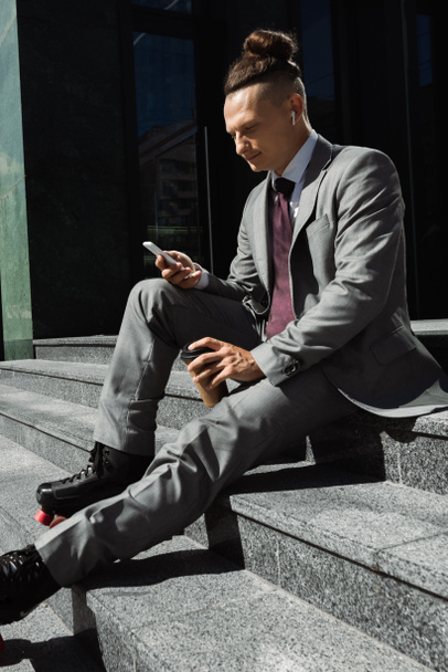 階段に座りながら紙コップを持っているローラースケートの若いビジネスマンやスマートフォンでメッセージを送る  - 写真・画像