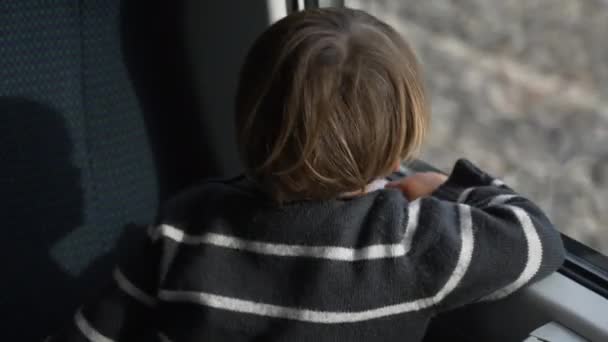 Jedno szczęśliwe dziecko podróżujące szybkim pociągiem gapiące się przez okno. Tył małego chłopca w szybkim pociągu w zwolnionym tempie - Materiał filmowy, wideo