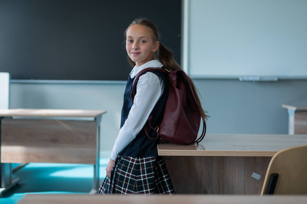 Portrait of a caucasian schoolgirl with a backpack in the classroom on the background of the school board - 写真・画像