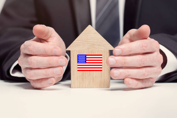 Businessman hand holding wooden home model with American flag. insurance and property concepts - Foto, Imagen