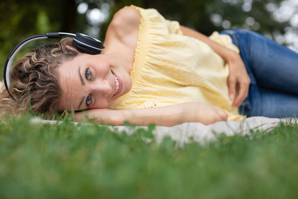woman listening to music with headphones lying on the grass - Foto, Imagen