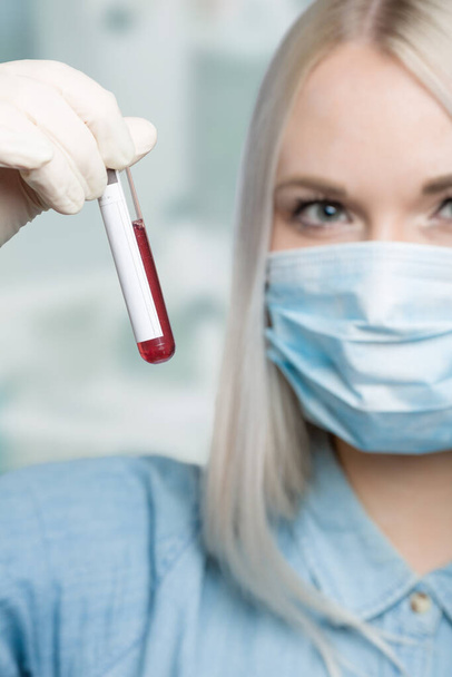 junge Frau mit medizinischer Gesichtsmaske und Handschuhen hantiert in einem Labor mit einer Blutsonde  - Foto, Bild