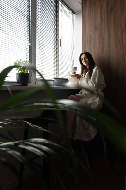 Μια γυναίκα πίνει καφέ το πρωί στο σπίτι. Όμορφο πρωινό στο άνετο σπίτι. - Φωτογραφία, εικόνα