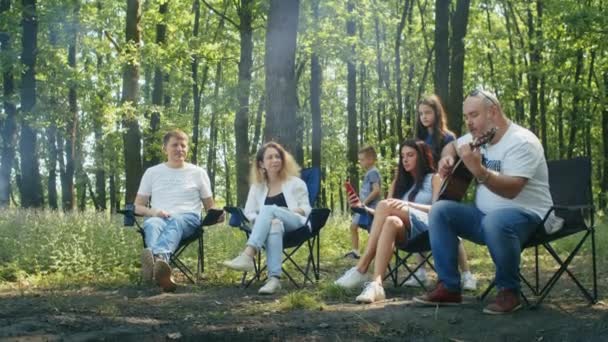Boldog társaság, anya, apa, fia, lánya és barátai piknikeznek az erdő környékén. családi kemping nyáron, pihenés sátorral a Forest City parkban - Felvétel, videó