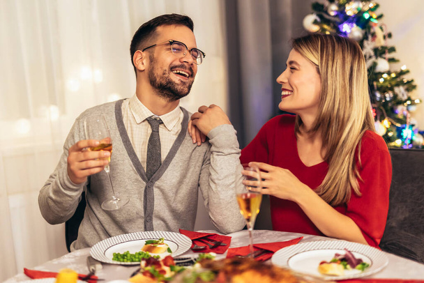 Ζευγάρι πίνοντας κρασί και γελώντας ενώ κάθεται γύρω από ένα τραπέζι κατά τη διάρκεια ενός δείπνου  - Φωτογραφία, εικόνα