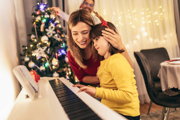 Молодые родители наслаждаются музыкой, которую их дочь играет на пианино во время Рождества - Фото, изображение