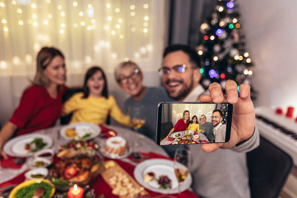 家庭で一緒にランチを楽しむ幸せな多世代の家族。家庭でのクリスマスディナーの家族は自撮り写真を作る. - 写真・画像