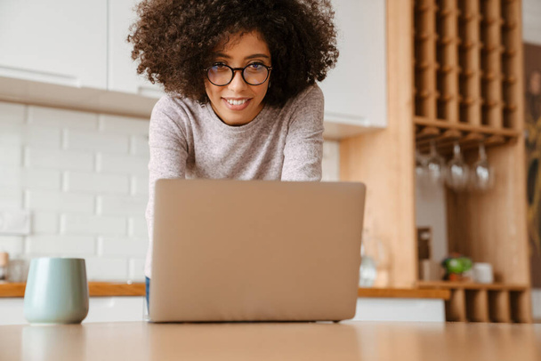 African american young woman with curly afro hairstyle and eyeglasses using laptop at home - Fotoğraf, Görsel