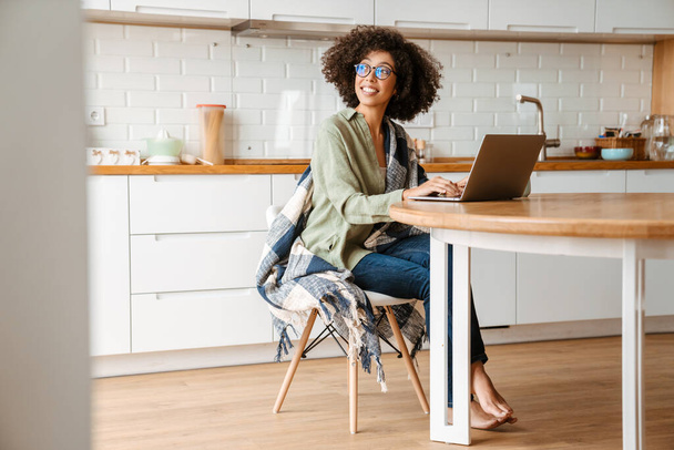 African american young woman with curly afro hairstyle and eyeglasses using laptop at home - Foto, Bild