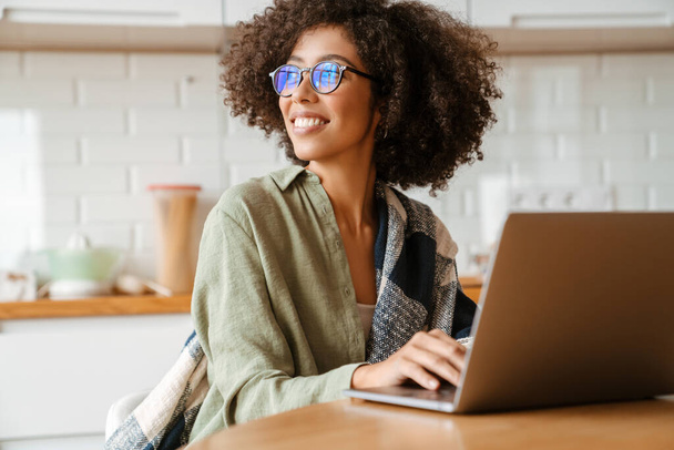African american young woman with curly afro hairstyle and eyeglasses using laptop at home - Foto, Imagem