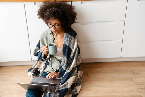African american young woman with curly afro hairstyle drinking coffee and using laptop at home - Foto, imagen