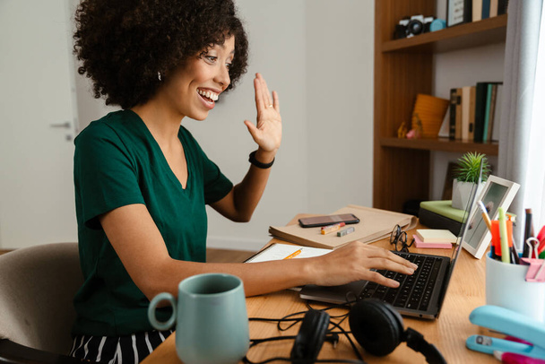 African american young woman with curly afro hairstyle sitting at desk and using laptop at home - Photo, Image