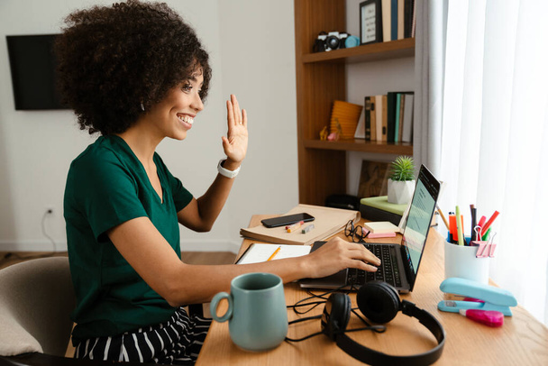 African american young woman with curly afro hairstyle sitting at desk and using laptop at home - Φωτογραφία, εικόνα