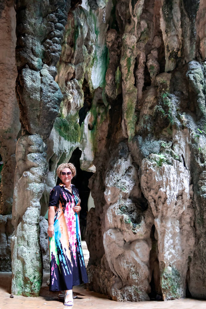 Una mujer bonita en un vestido de color largo sobre un fondo de rocas de colores en las cuevas de Batu en Gombak, Selangor, Malasia - Foto, Imagen