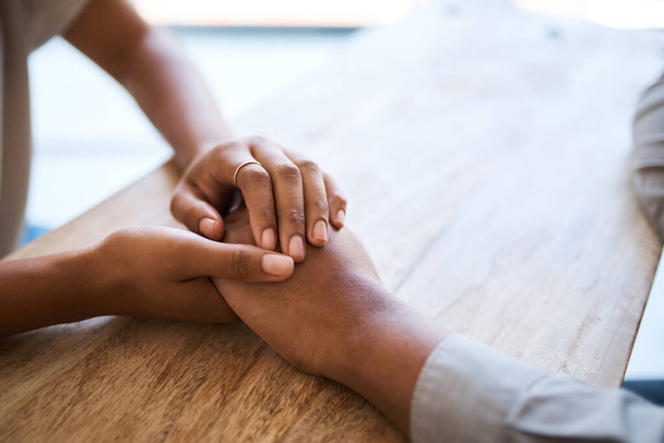 Paar, hand in hand en steun op tafel in close-up voor hulp, zorg en empathie in tijden van verdriet. Zwart paar, helpende hand en liefde om te vergeven, te raadplegen of comfort samen in huis met vriendelijkheid. - Foto, afbeelding
