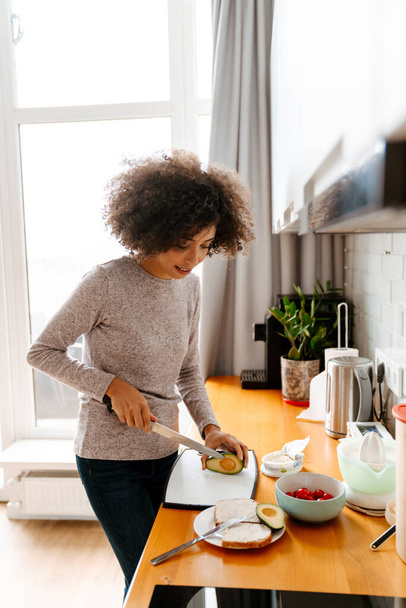 African american young woman with curly afro hairstyle making breakfast in morning at home - Fotografie, Obrázek