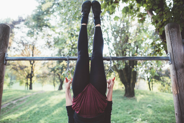 Onbekende sportieve fit jonge vrouw oefenen voor kracht en evenwicht in een outdoor fitness park - Foto, afbeelding