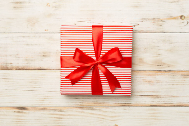 Gift box with red ribbon bow on wooden background, top view. - Photo, Image