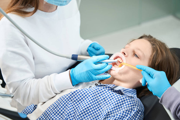 Young patient treats a tooth at a dentist in a medical institution, the doctor uses an endomotor in his work - Foto, Imagen