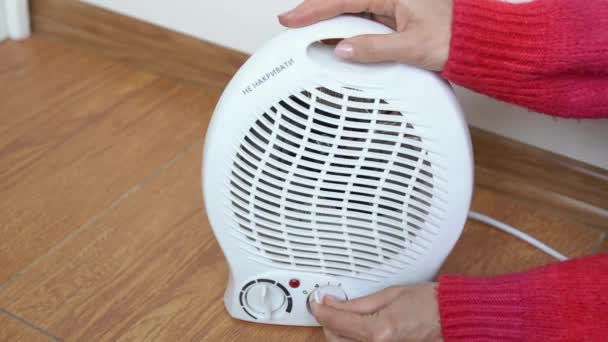 Woman hands in a red sweater adjusting electric fan heater in room and checks with his hand if there is heat. Girl turns on the portable fan heater to heat the room. Autonomous electric space heating - Footage, Video