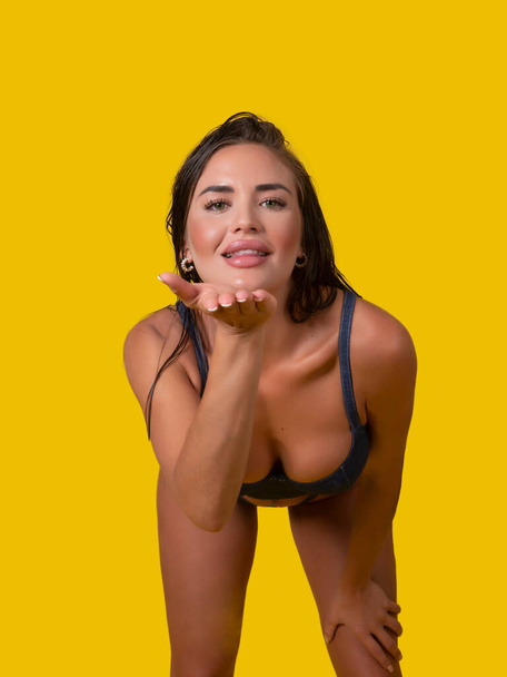 Glad female model in underwear smiling and blowing air kiss to camera against yellow background - Photo, Image