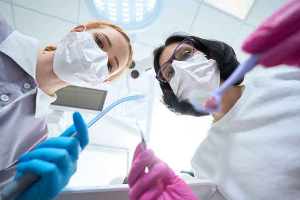 Dvě ženy v ochranných maskách v procesu zubní manipulace, používají zavlažovač - Fotografie, Obrázek